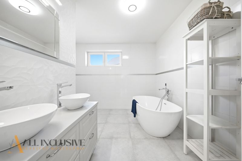 A bathroom in a family house with a bathtub, two sinks, and a shelf.