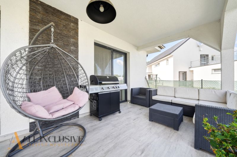 A terrace of a family house with comfortable rattan seating and a grill on a floor with a wooden decor.