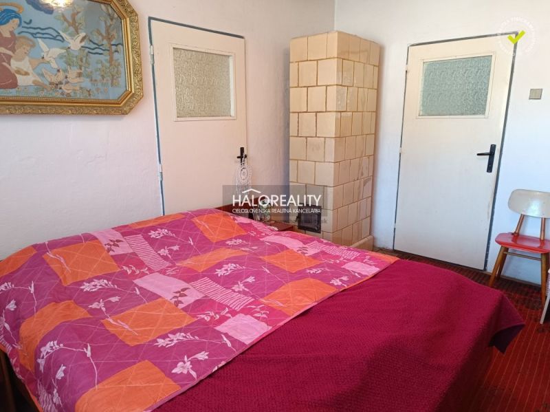 A bedroom in a family house with a tiled stove, a painting, and a chair.