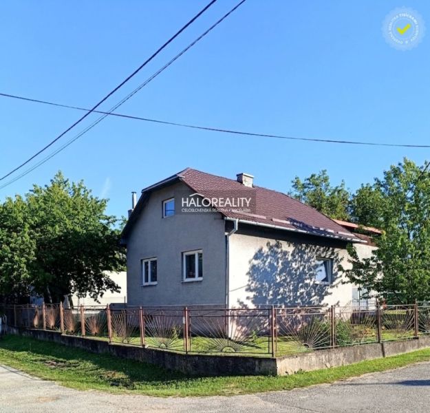 A family house in Margecany with a sloped roof, fenced, surrounded by greenery and a blue sky.
