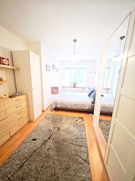 A bright bedroom in a two-room apartment with wood-patterned flooring and a mirrored wardrobe.