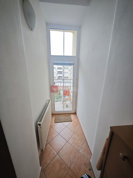 A narrow hallway with a window and a radiator in a 2-room apartment, tiles on the floor.
