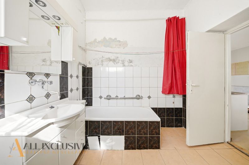 A bathroom in a family house with a bathtub, white tiles, and a red curtain.