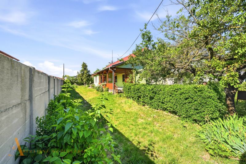 A family house in Hviezdoslavov with a garden, green shrubs, and a grassy plot by a concrete fence.