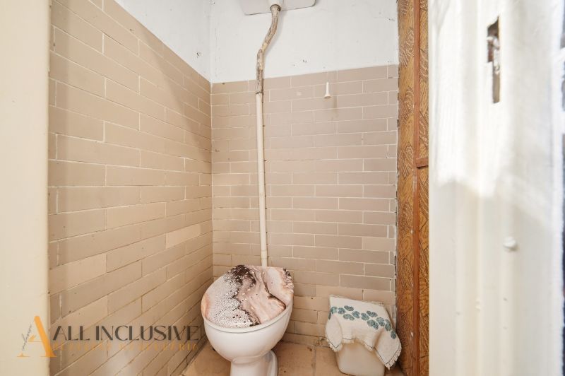 A simple bathroom with a toilet tiled in beige tiles in a family house.