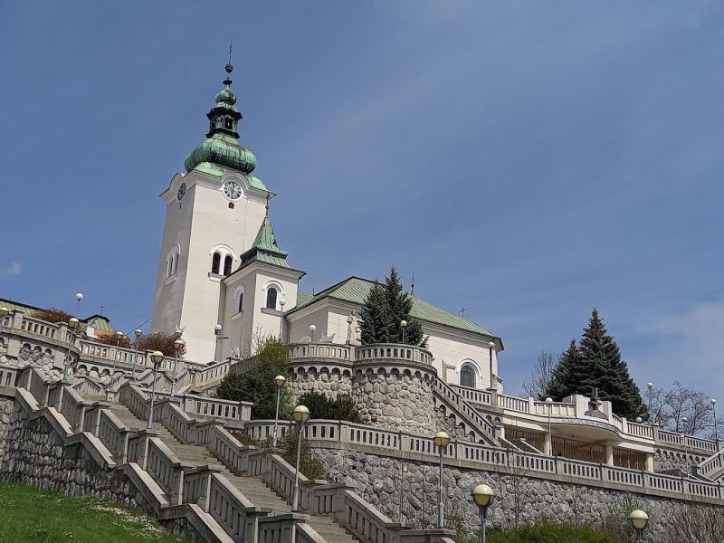 A church with a tower surrounded by a staircase and greenery in Ružomberok.