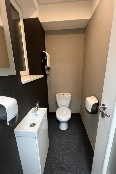 A toilet with a sink and a paper dispenser in offices.