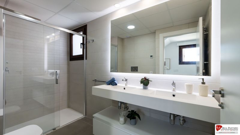 A bathroom in a 2-room apartment with a double sink, mirror, and shower enclosure.