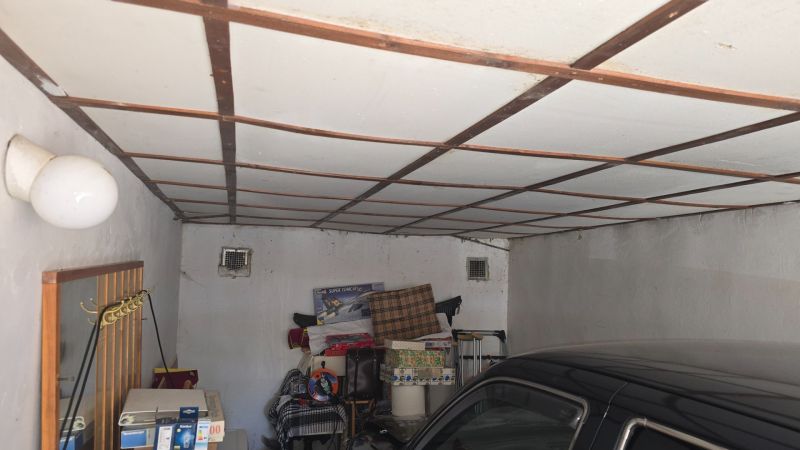 A garage with a white fan, stored items, and a parked car.