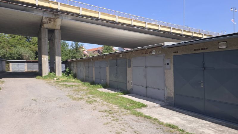Garages on Jesenského Street in Zvolen under the bridge, surrounded by greenery and a gravel road.