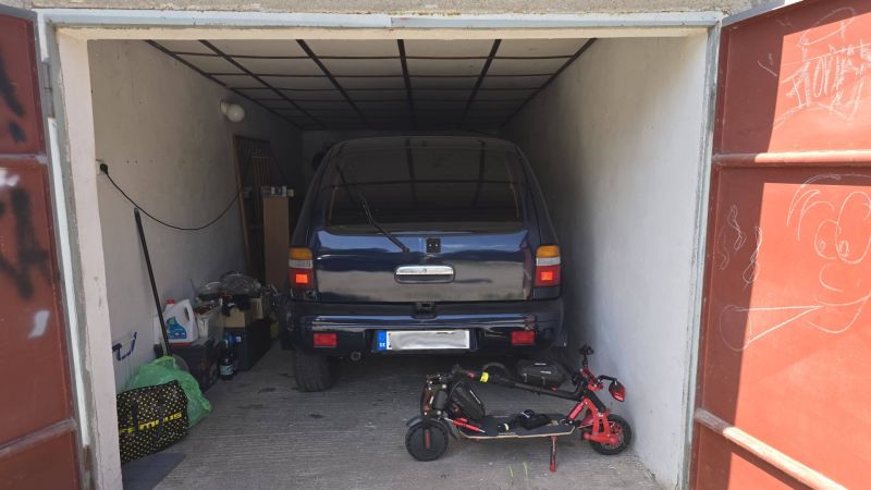 A garage with a car and an electric scooter, stored items, and a drawing on the door.