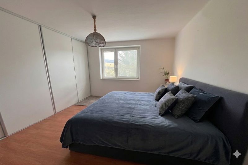 Bedroom in a family house with a bed, wooden decor flooring, and a built-in wardrobe.