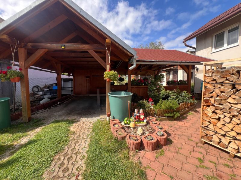 A family house in Bacúch with a shelter, a garden, and stored wood, sunny day.