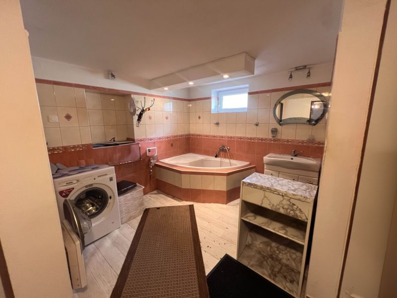 A bathroom in a family house with a bathtub, washing machine, sink, and a floor with a wooden decor.