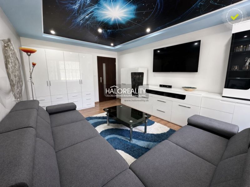 Living room in a studio apartment with a dark gray sofa, glass table, and wood-patterned flooring.
