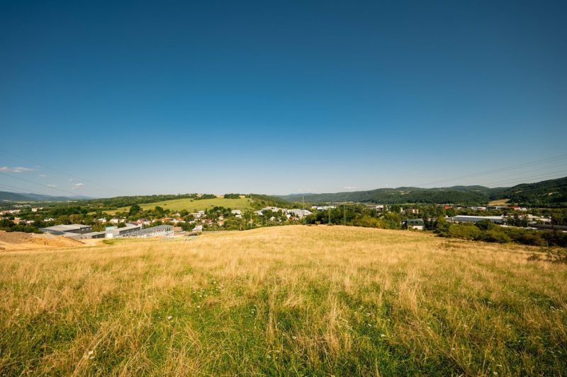 A landscape with a grassy meadow and a village in the background in the Banská Bystrica district, Banskobystrický region, suitable for residential plots.