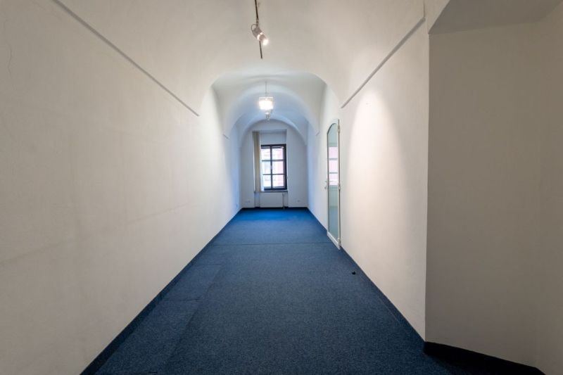 A narrow corridor with a curved ceiling, carpet, and a large window at the end.