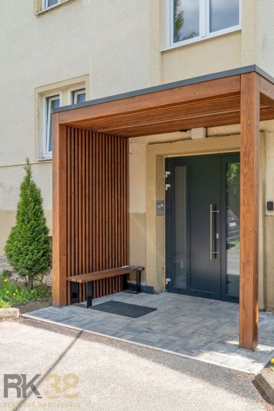 Entrance to an apartment building in Poprad with a wooden shelter and a bench.