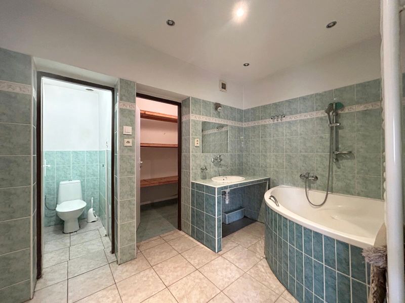 A bathroom in a family house with a bathtub, green tiles, and access to a toilet.