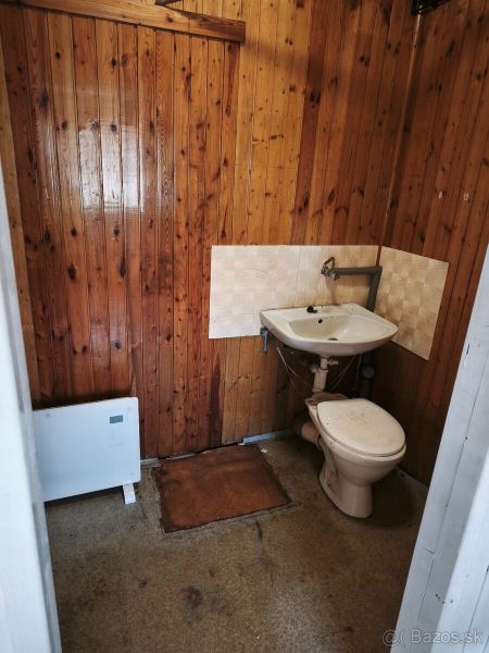 A restroom with wooden wall paneling and a simple sink in commercial premises.