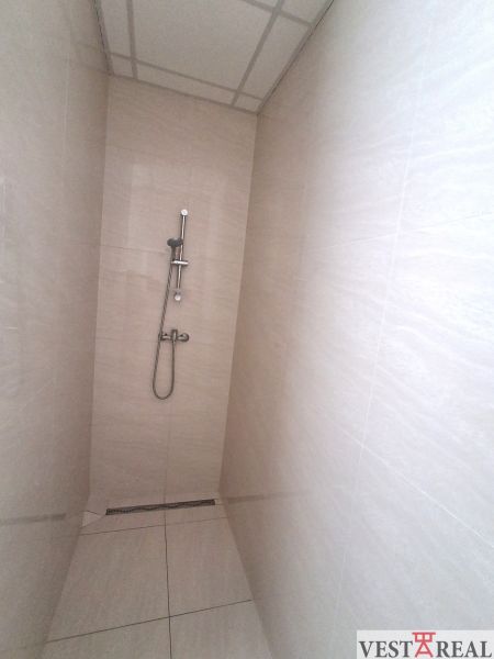 Shower enclosure in the office with tiles and a stainless steel shower.