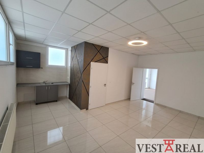 An office space with a kitchenette and a light floor with a wall decoration.