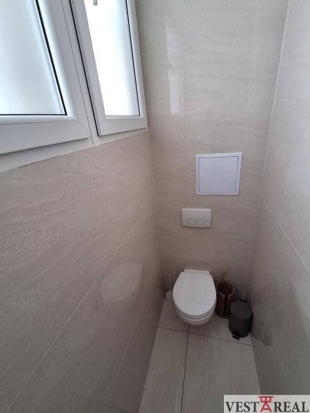 A bathroom in the office with a closed toilet and simple tiles.
