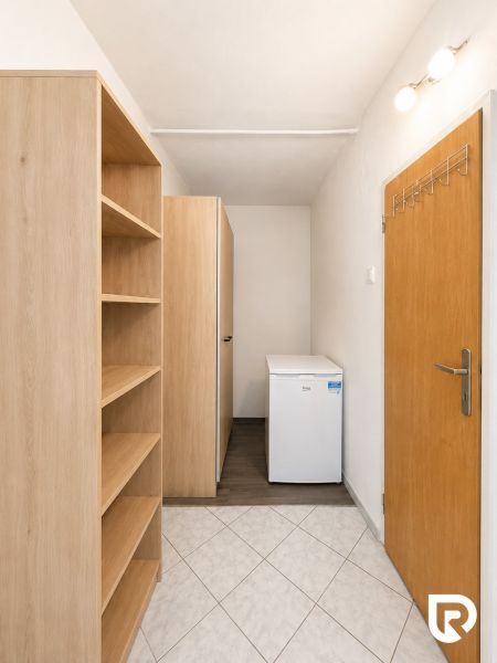 A hallway with a white floor, a shelving cabinet, and a small refrigerator, a 3-room apartment.