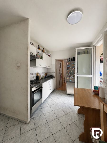 A kitchen in a 3-room apartment with a kitchen unit, stove, and table on tiles.