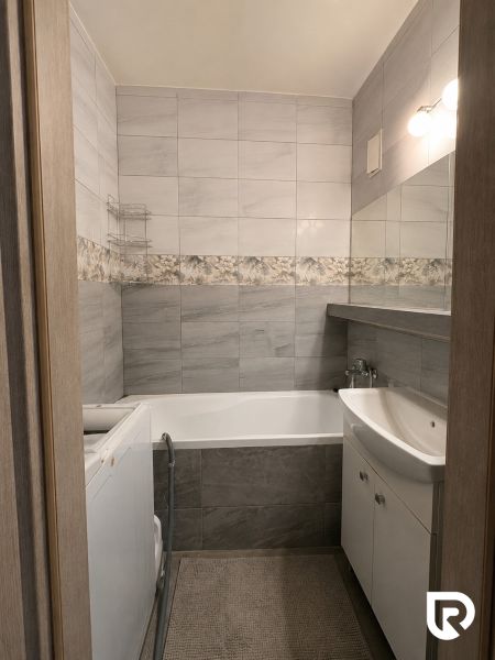 A bathroom in a 3-room apartment with gray tiles, a bathtub, and a washing machine.