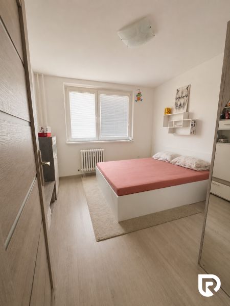 A bedroom in a 3-room apartment with a wooden decor floor and a simple bed.
