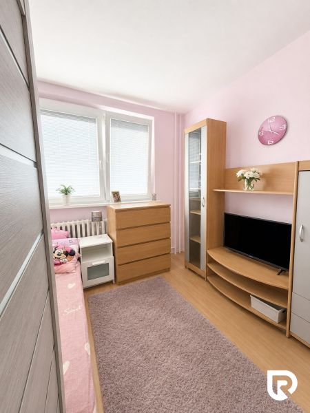 Children's room with wood-patterned flooring, pink walls, and wooden furniture in a three-room apartment.