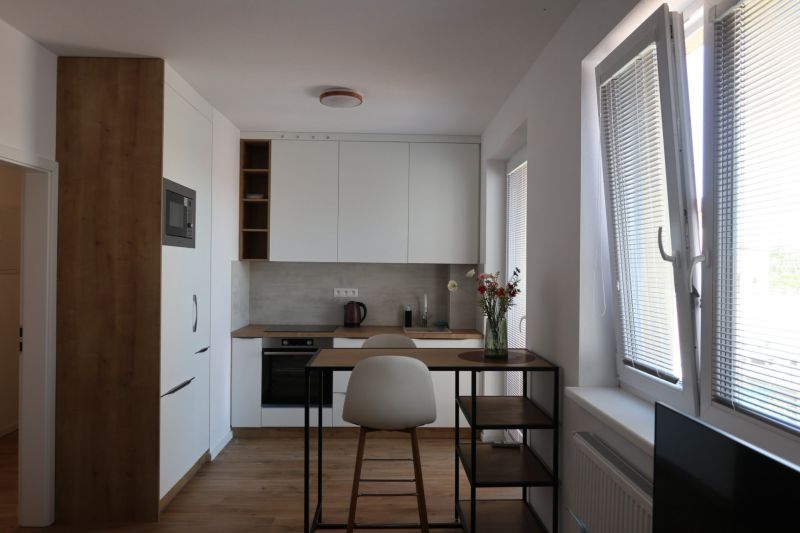 A kitchen in a 2-room apartment with a wood-patterned floor, arched windows, bar table.