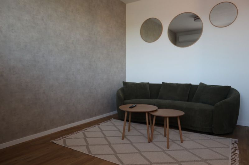 Living room in a two-room apartment with a green sofa, round tables, and three mirrors.