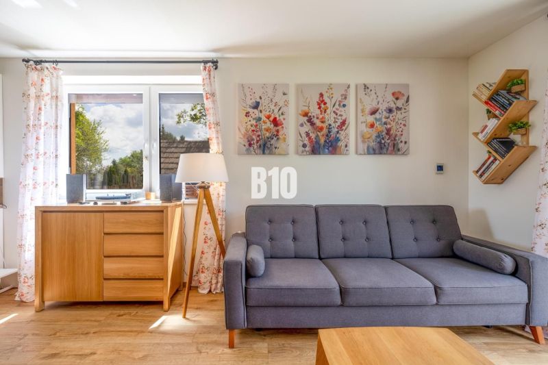 Living room with a sofa, paintings, and a wooden-patterned floor in a family house.