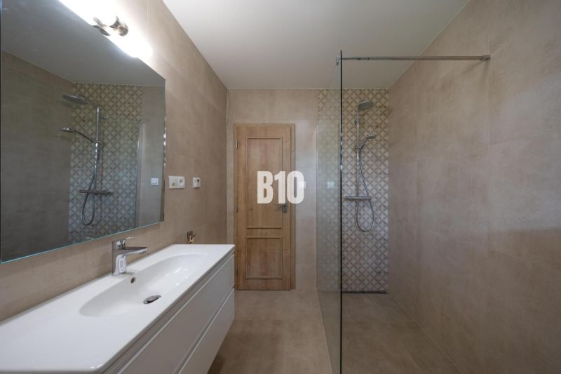 Modern bathroom with a large mirror, shower stall, and minimalist furnishings.
