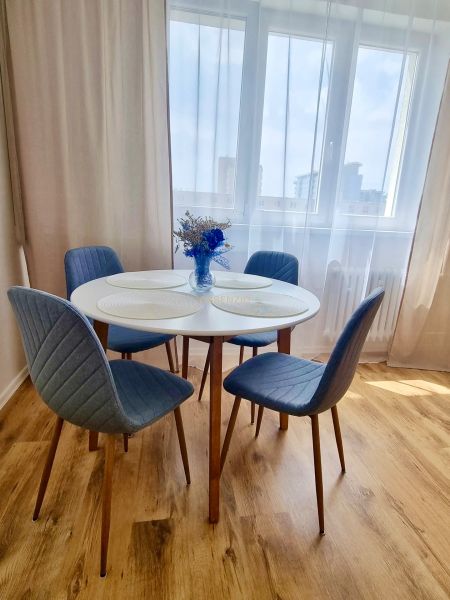 Dining area with a round table, blue chairs, and a wood-patterned floor.