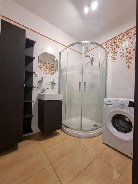 Bathroom in a 2-room apartment with a washing machine, shower corner, and tiled floor.