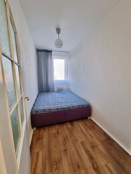 A simple bedroom with a bed, neutral walls, and a wooden decor floor in a 2-room apartment.