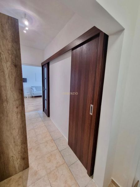 A hallway with sliding doors, tiles, and a view into the living room in a 2-room apartment.