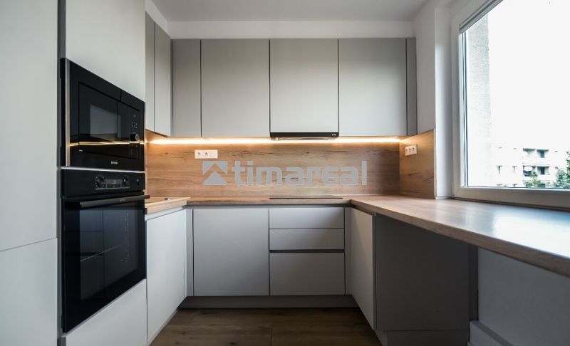A kitchen with built-in appliances, light cabinets, and a wood-patterned floor in a three-room apartment.