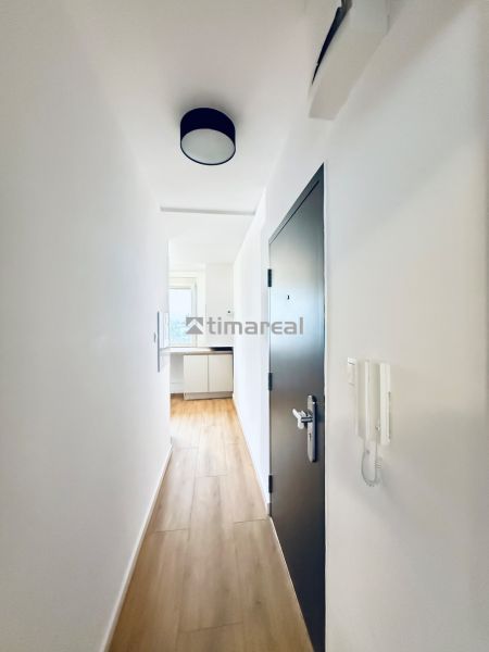 A corridor with a light interior, white walls, and a floor with a wood decor.