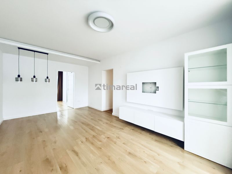 Living room of a three-room apartment with white furniture and a wooden decor floor.