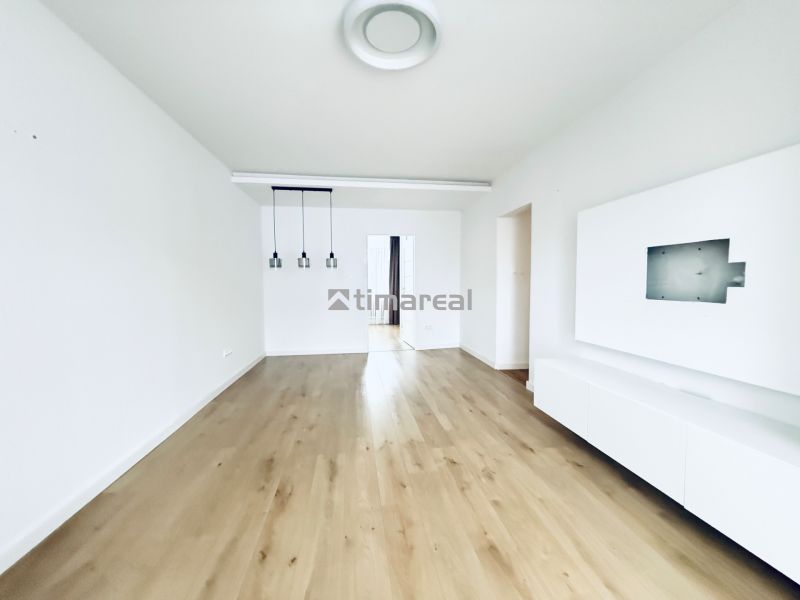 Living room in a three-room apartment with white walls and a floor with a wooden decor.