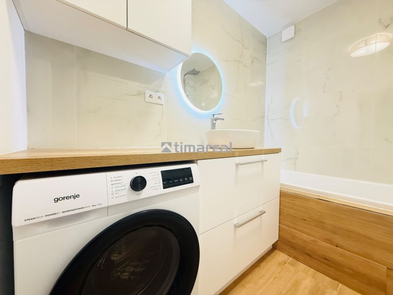 Bathroom in a 3-room apartment with a washing machine, sink, and bathtub, floor with wooden decor.