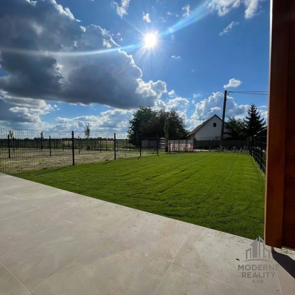 A garden with a lawn and paving at a family house in Andovce on a sunny day.