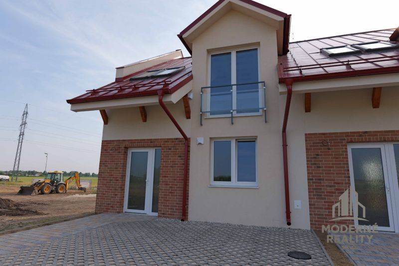 A family house in Andovce with a brick cladding and a red roof, excavator in the background.