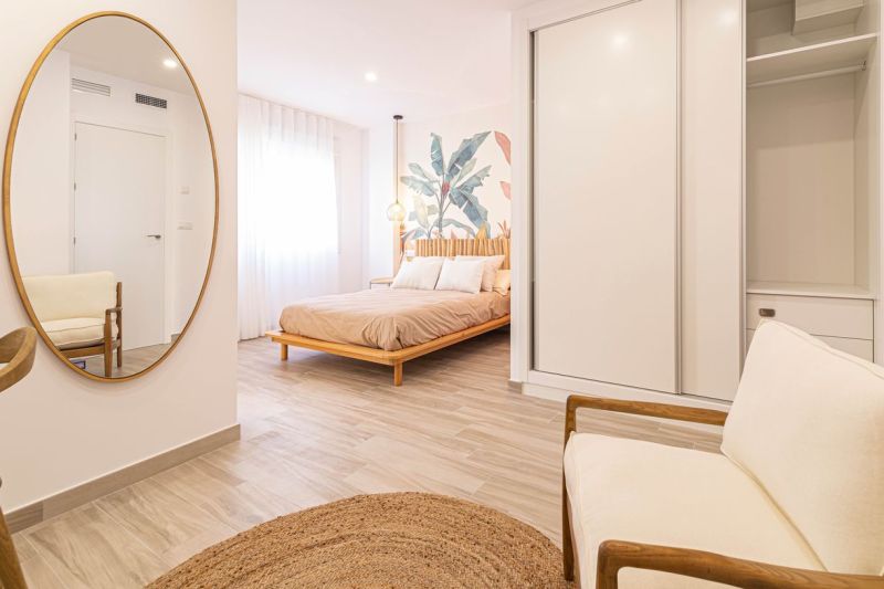 Interior of a holiday apartment with a bed, mirror, and wooden decor flooring.