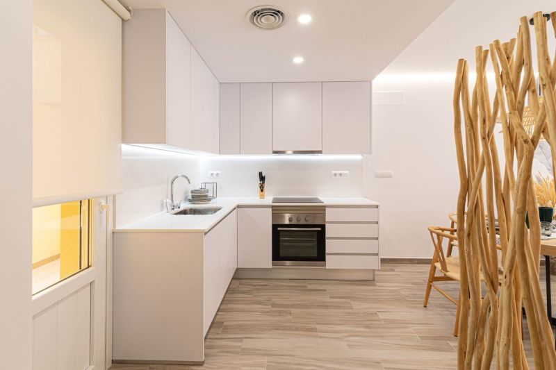 A kitchen in a holiday apartment with white cabinets and wood-patterned flooring.