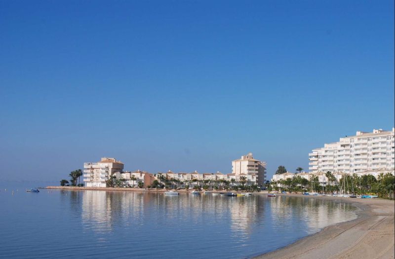 The coast with holiday apartments in La Manga del Mar Menor by the calm sea and blue sky.
